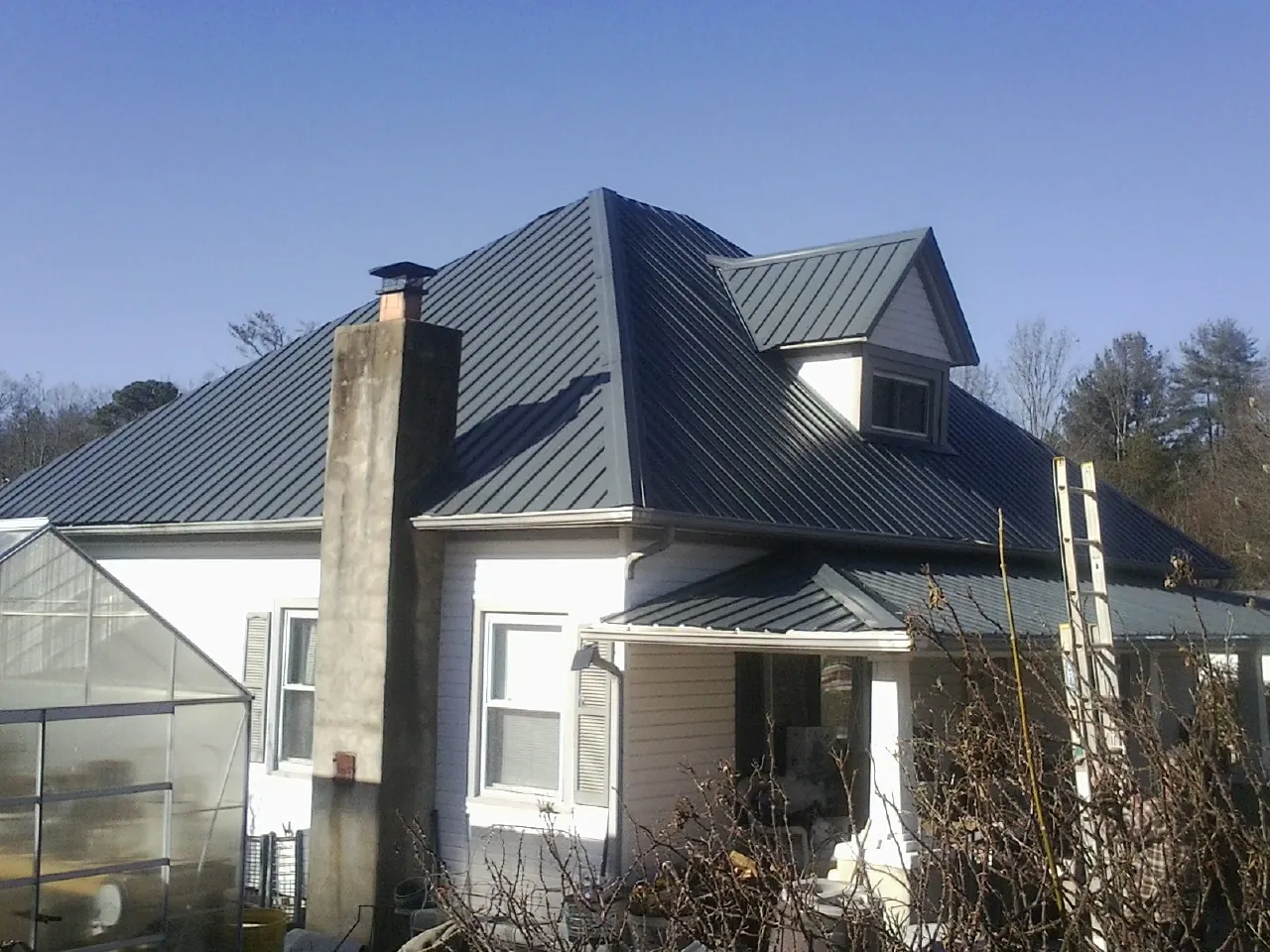 Dark blue standing seam metal roof on a white farmhouse with dormer — Slate & Tile Roof Repair by Roofing Brothers in Glenolden