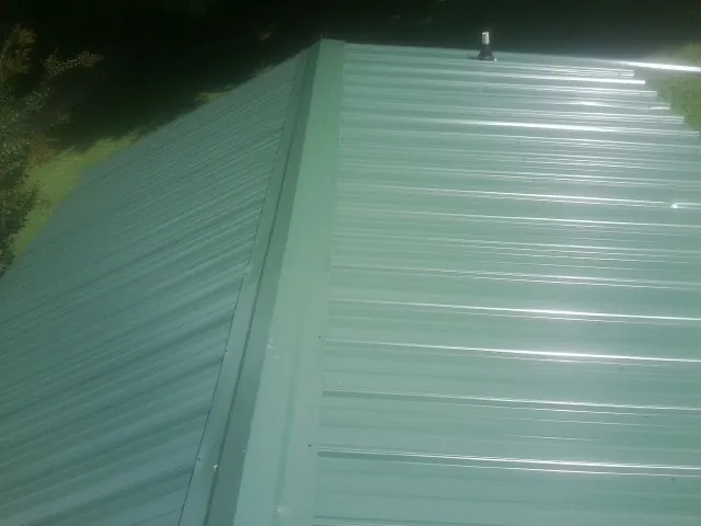 New green metal panels meeting at the ridge of a roof — Flat Roof Repair work by our crew in Glenolden