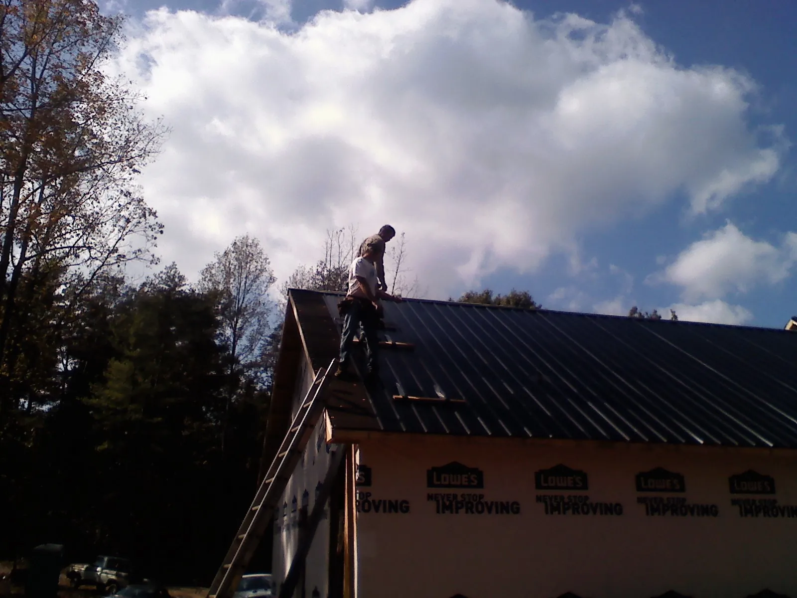 Roofer fastening dark metal panels high against a cloudy sky, from a Roof Inspection job in Glenolden