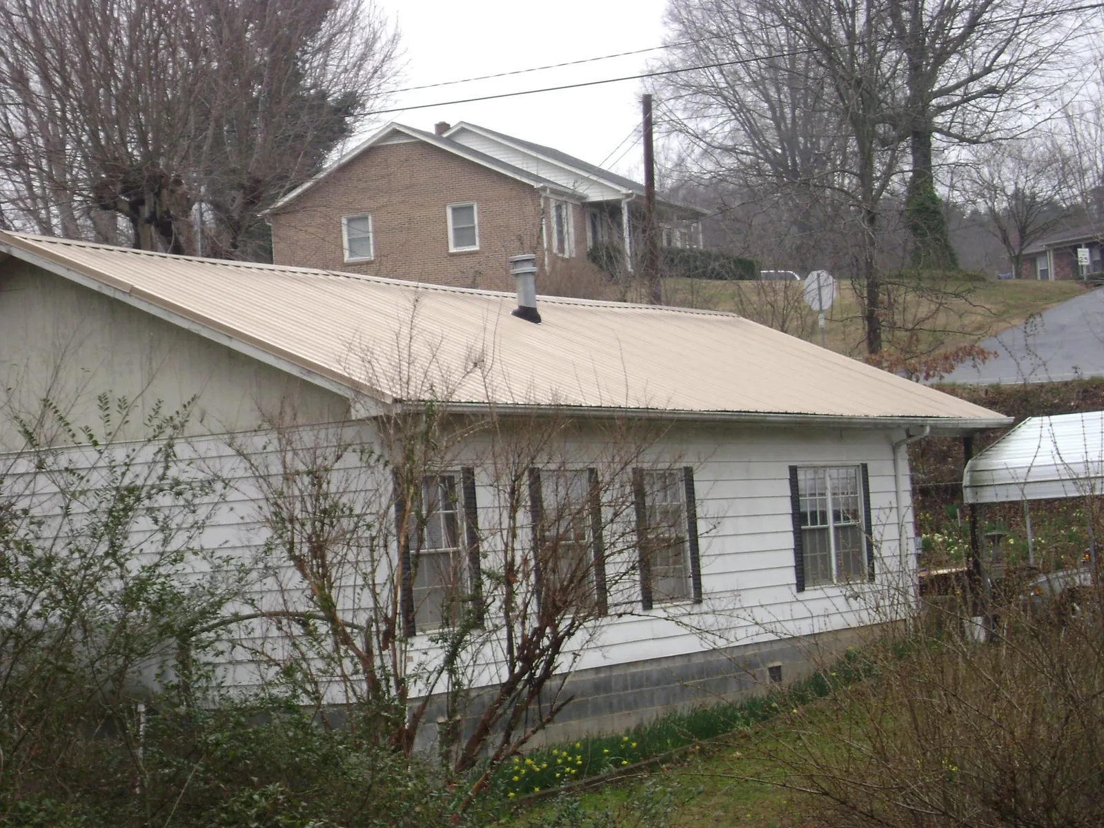 Tan metal roof on a white sided house set into a hillside — Commercial Roofing by Roofing Brothers in Glenolden